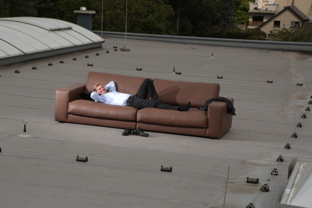 Ralf Tenbeck liegt auf einem Sofa, das auf dem Dach vom Möbelhaus Möbel Kerkfeld steht.