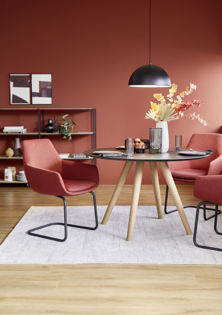 Ein Esszimmer mit Tapete in rötlichem Herbst ton, roten Stühlen einem runden Tisch und der Pendelleuchte KIA.